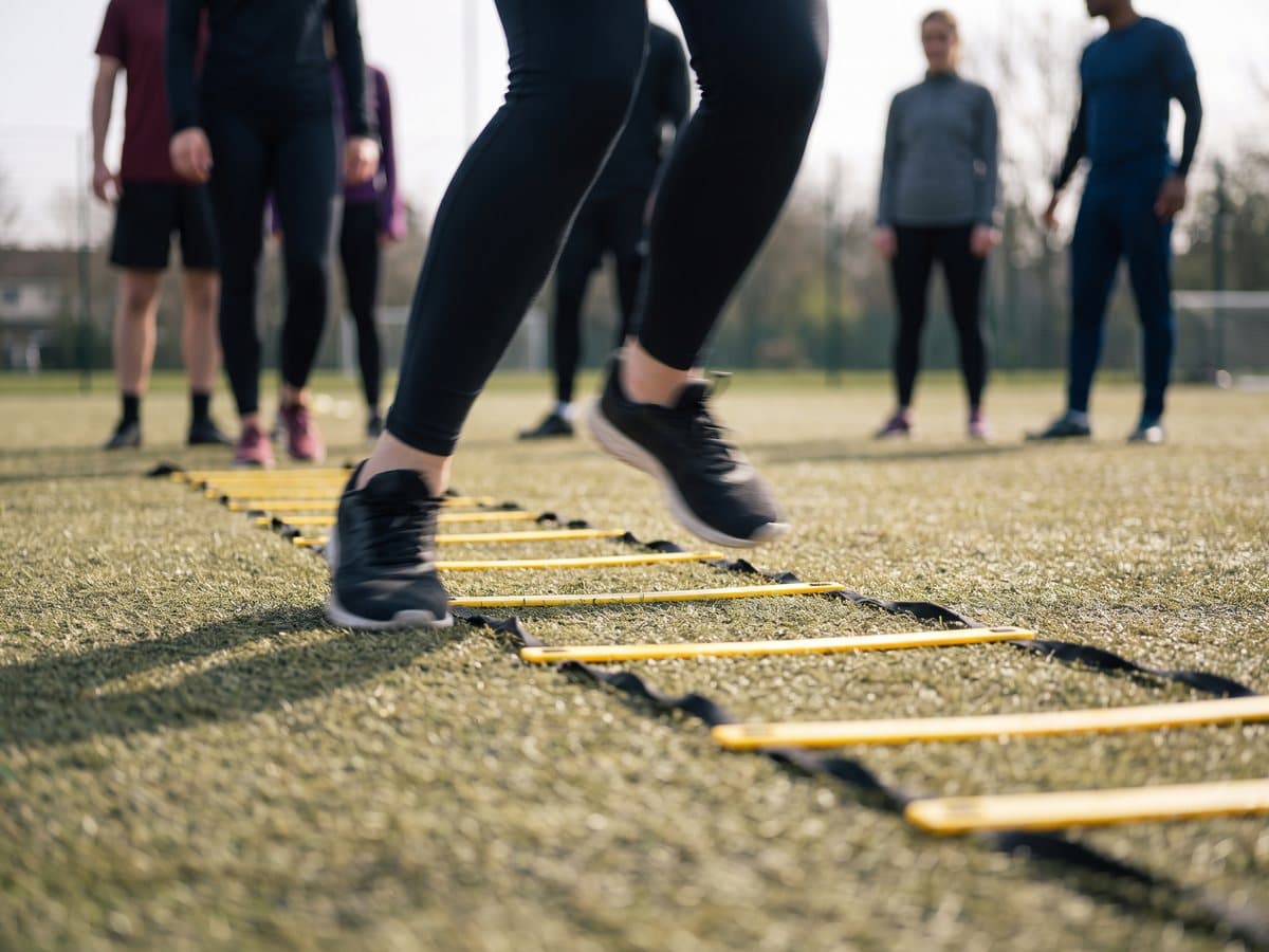 An athlete stepping quickly through a yellow agility ladder laid on artificial turf, seen from a low angle